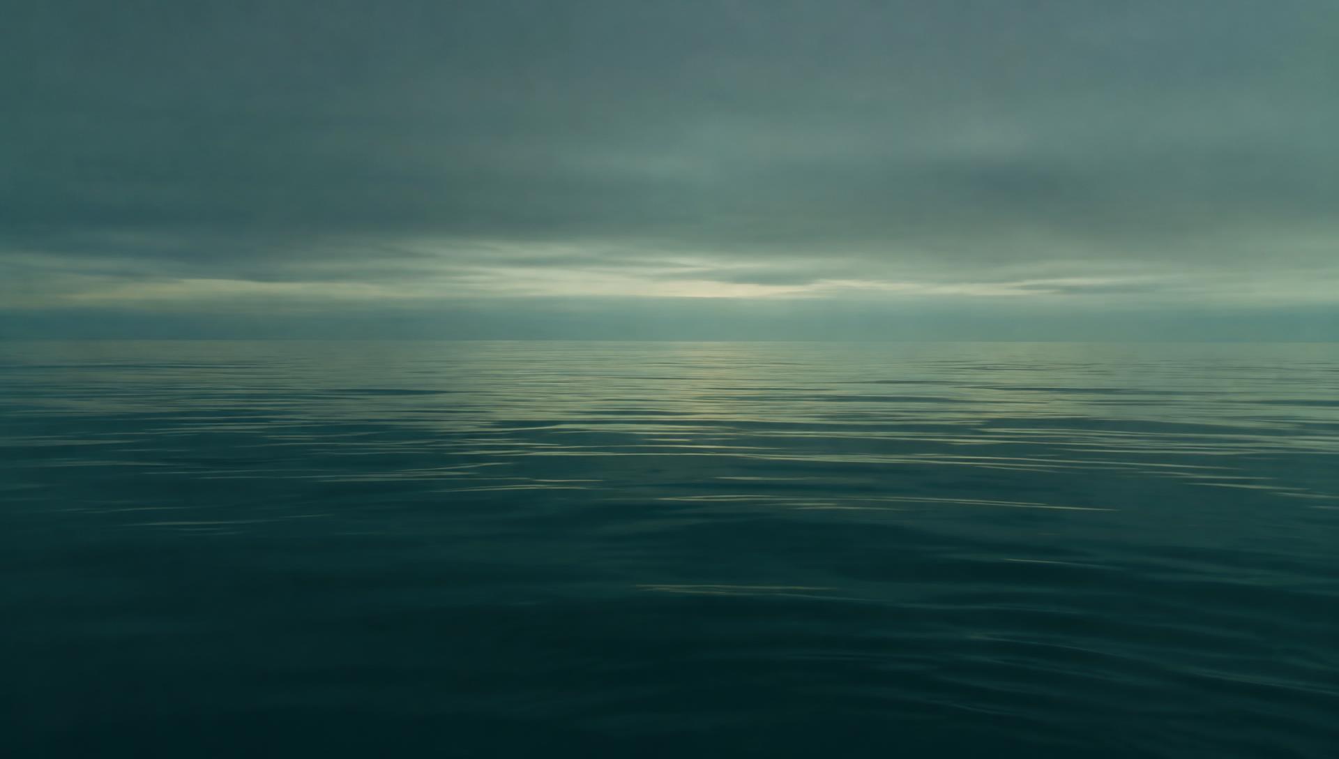 A calm, still water surface under a grey dawn sky